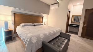 Ein modernes Schlafzimmer mit einem großen Bett, Nachttischen, einer Bank und einem durch eine offene Tür einsehbaren Badezimmer.