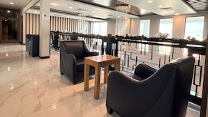 Eine moderne Lobby mit Marmorboden, schwarzen Ledersitzen, einem Holztisch und einer dekorativen Geländer.