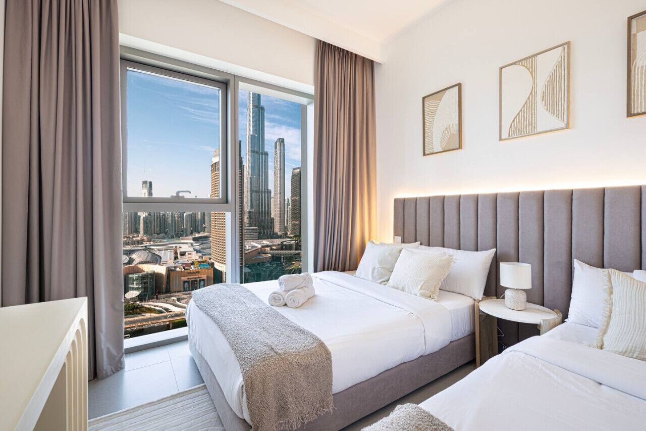 Ein Hotelzimmer mit einem großen Bett, einem Nachttisch und Blick auf eine Stadtlandschaft durch ein großes Fenster.