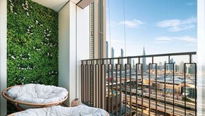 A balcony with two wicker chairs, a green wall with white flowers, and a cityscape view.