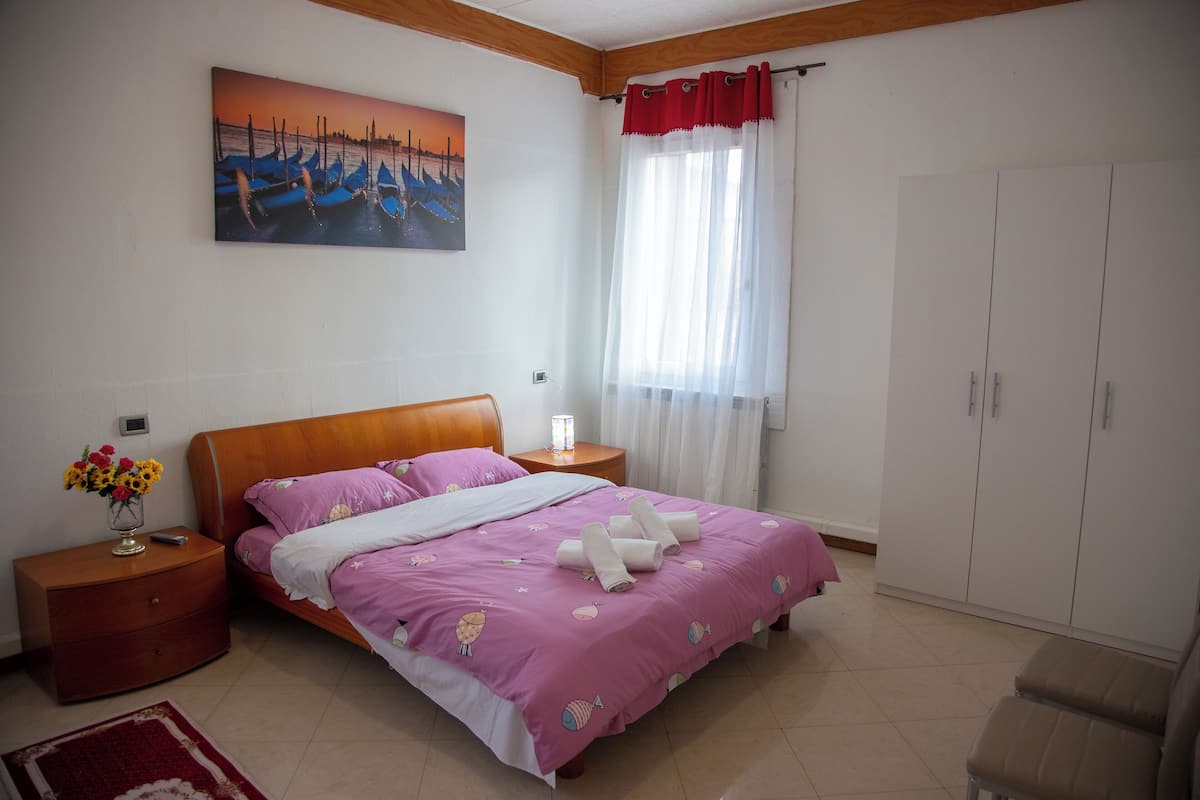 A bedroom with a bed, nightstands, a dresser, a wardrobe, a painting, and a window with curtains.