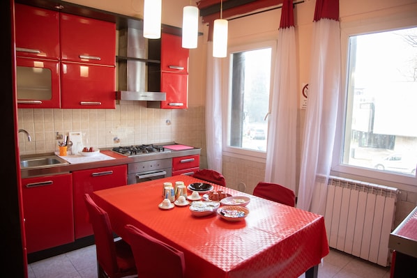 A kitchen with red cabinets, a stove, and a dining table set with various dishes. - CA RIZZARDI (Mestre)