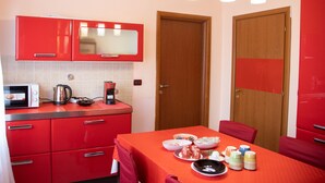 A compact kitchen with red cabinets, a microwave, a coffee maker, and a dining table set with plates and bowls. - CA RIZZARDI (Mestre)