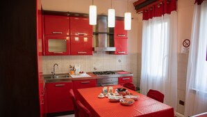 A kitchen with red cabinets, a gas stove, and a dining table set for four. - CA RIZZARDI (Mestre)
