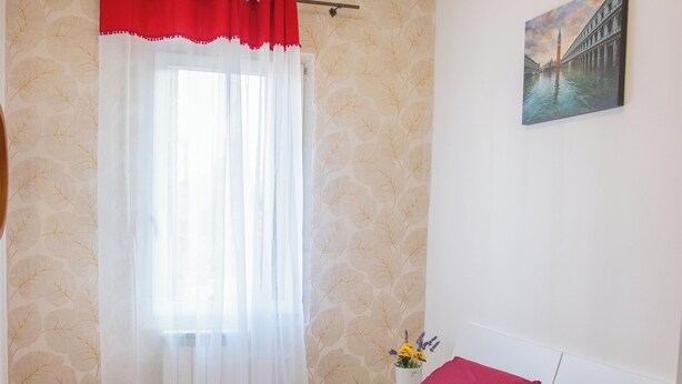 A hotel room with two beds, each with red bedding and white pillows, a window with sheer curtains, a painting on the wall, and a vase with flowers on the nightstand. - CA RIZZARDI (Mestre)
