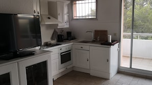 Cocina compacta con armarios blancos, horno empotrado, cafetera y ventana con vistas a un balcón.