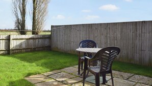 A patio with two chairs and a table, surrounded by a wooden fence and a grassy lawn. - Byre Cottage - Meadowbrook Farm (Moreton, near Thame)