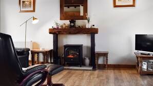 A cozy living room with a fireplace, a black leather chair, a wooden coffee table, and a television. - Byre Cottage - Meadowbrook Farm (Moreton, near Thame)