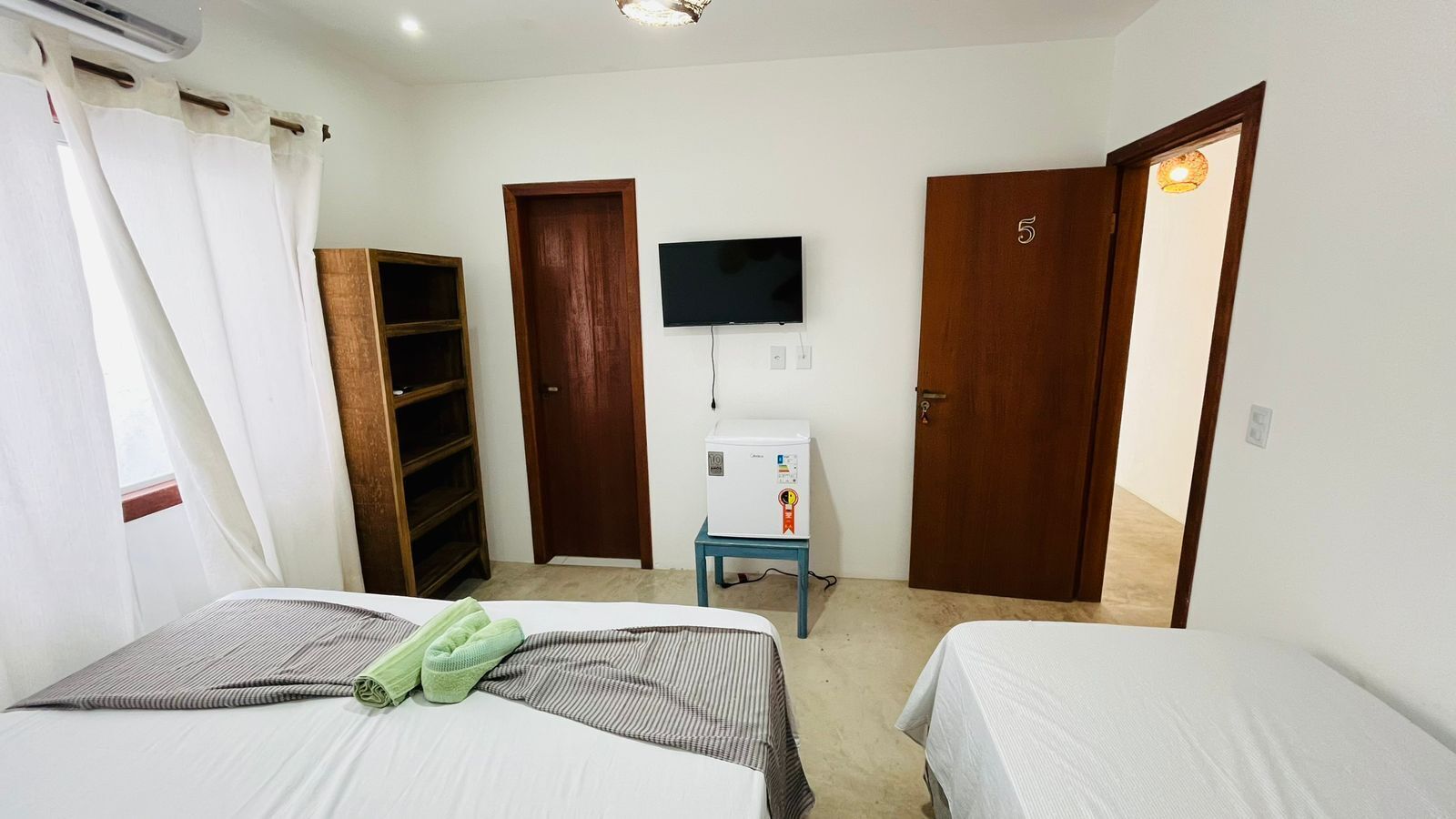 Una habitación con dos camas, televisor, una mesita con refrigerador y un armario de madera.