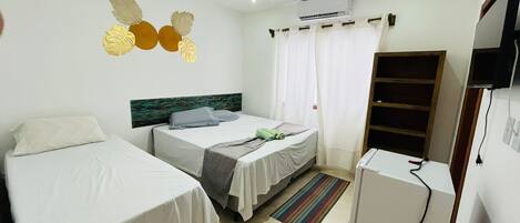 A room with two single beds, a small desk, an air conditioner, a TV, and a bookshelf.