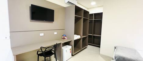 Quarto com cama, escrivaninha com cadeira, televisão fixada na parede e guarda-roupa.