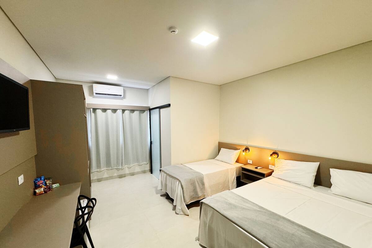 Una camera d'albergo con due letti, una scrivania, una sedia e una televisione.