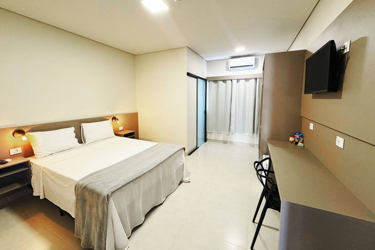 Camera d'albergo con un letto, comodini, una scrivania, una sedia, una TV a parete e un condizionatore d'aria.