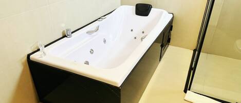 Un baño moderno con una bañera blanca, lavamanos negro y mampara de cristal.