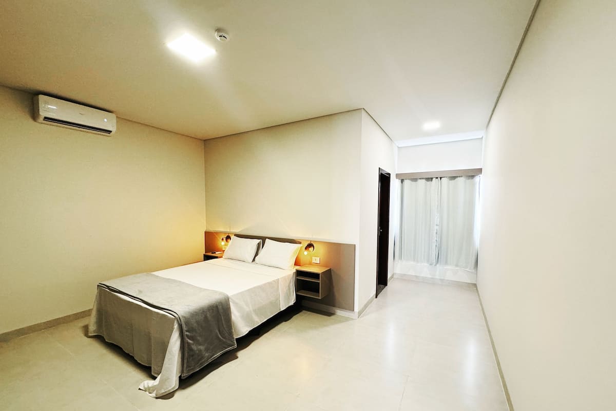 Una moderna camera d'hotel con un letto, comodini, un condizionatore d'aria e vista su un balcone.