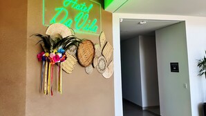A hotel reception area with a neon sign reading "Hotel da Vila," decorative woven baskets, and a sign indicating a smoking area.