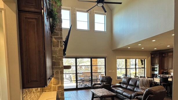 A spacious living area with a stone fireplace, dark wood flooring, leather sofas, and a ceiling fan. - New Lake Paradise! 4 bdrm 3.5 ba house w/ lift, deck, grill, sauna, smart, media (Tool)