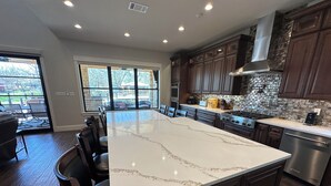 A modern kitchen with a large island, dark wood cabinets, and a stone backsplash. - New Lake Paradise! 4 bdrm 3.5 ba house w/ lift, deck, grill, sauna, smart, media (Tool)