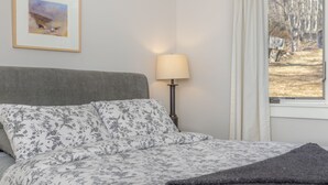 A bedroom with a bed, a lamp, a window with curtains, and a framed picture on the wall.