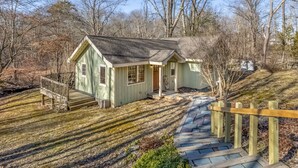 A small, single-story house with a green exterior and a wooden deck leading to the front door.