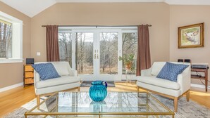 A modern living room with two white sofas, a glass coffee table, and a large window with curtains.