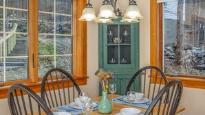 A dining area with a wooden table set for four, surrounded by chairs, with a green cabinet and hanging lights in the background.
