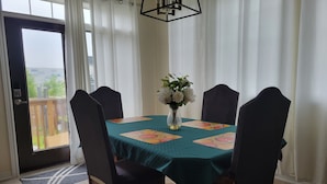 A dining area with a table set for four, chairs, a vase with flowers, and a view through a glass door. - Jack and Jill private suite, safe and relaxing 2 bedroom apartment @ RoseGlen  (Niagara-on-the-Lake)