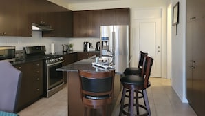 A modern kitchen with dark wood cabinets, stainless steel appliances, a central island with bar stools, and a visible door leading to another room. - Jack and Jill private suite, safe and relaxing 2 bedroom apartment @ RoseGlen  (Niagara-on-the-Lake)