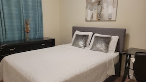 A neatly made bed with a white quilted bedspread, two pillows, a small bedside table, and a wall-mounted abstract painting. - Jack and Jill private suite, safe and relaxing 2 bedroom apartment @ RoseGlen  (Niagara-on-the-Lake)