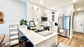 A modern kitchen with white cabinets, stainless steel appliances, a central island with bar stools, and a small potted plant.