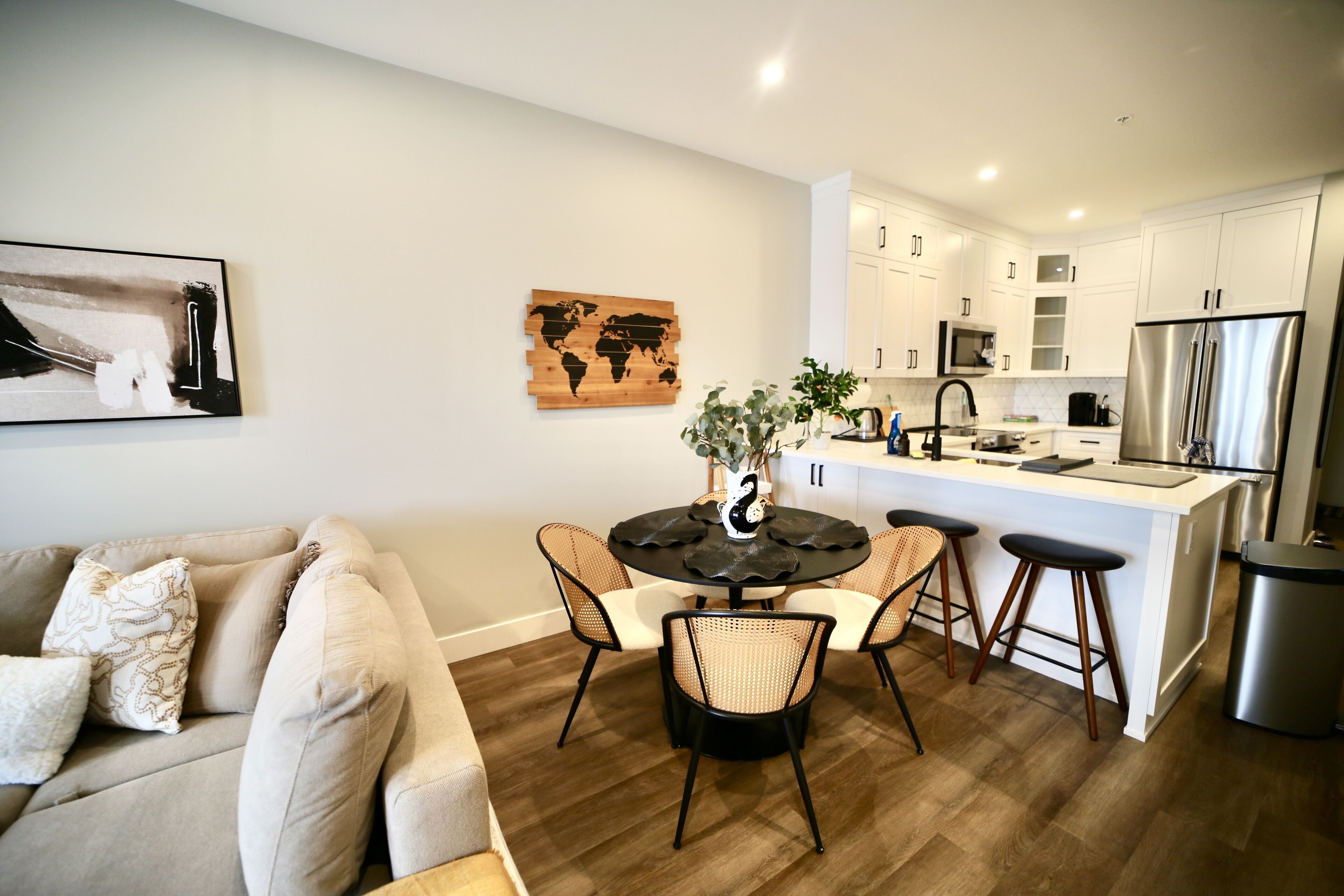 A modern kitchen with white cabinets, a stainless steel refrigerator, and a dining area with a round table and chairs.