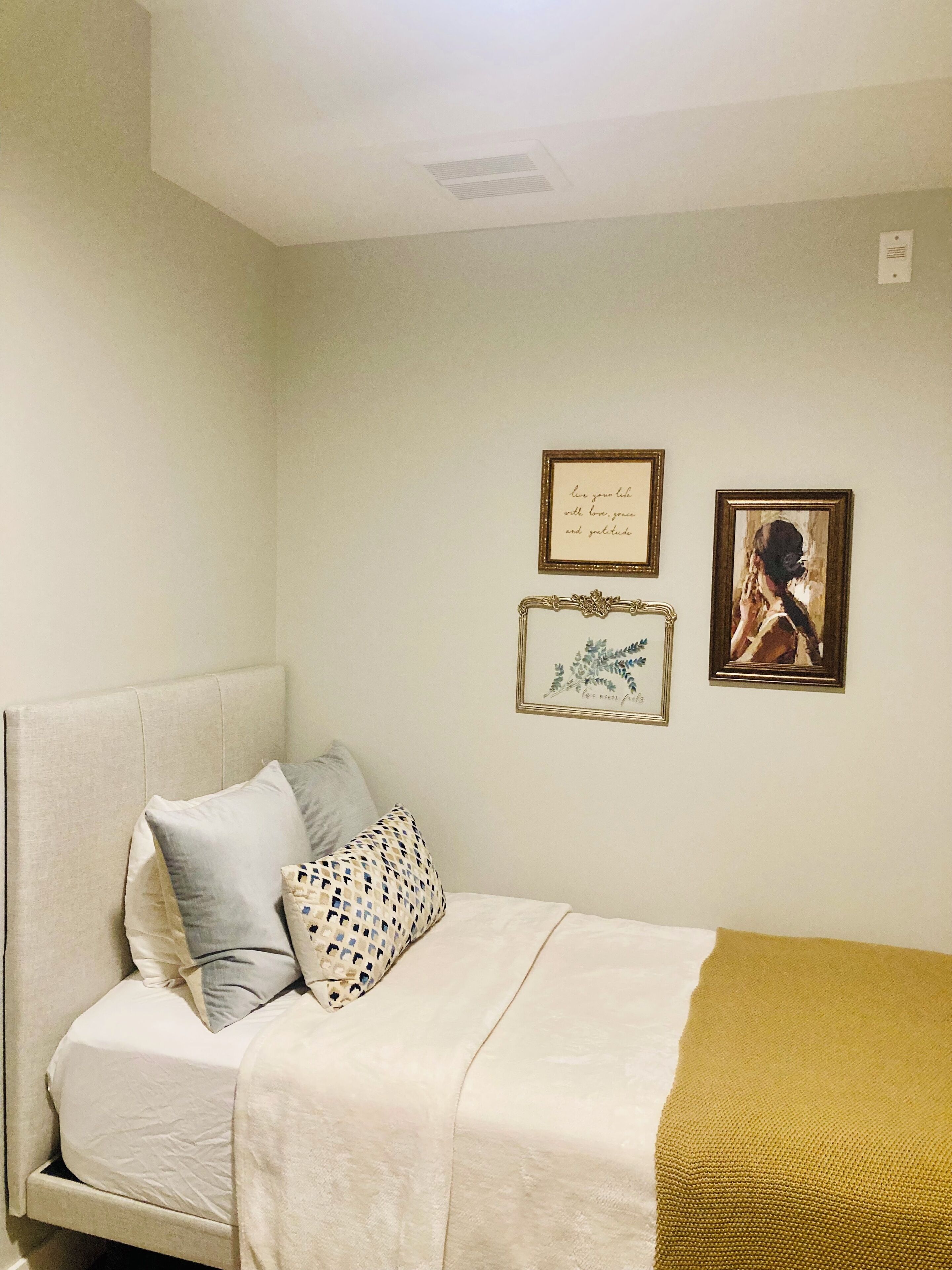 A bedroom with a bed, pillows, a blanket, and two framed pictures on the wall.