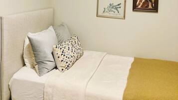 A bedroom with a bed, pillows, a blanket, and two framed pictures on the wall.