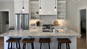 A modern kitchen with a central island, bar stools, a stainless steel refrigerator, and pendant lighting.