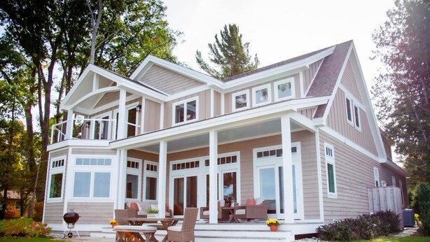 A two-story house with a covered porch, large windows, and a barbecue grill in the yard.
