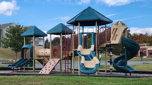 Ein Spielplatz mit mehreren Rutschen und Klettergerüsten, umgeben von einer Rasenfläche und Wohngebäuden.