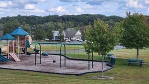 Ein Spielplatz mit Rutschen und Schaukeln, umgeben von einer Rasenfläche und Bäumen.