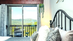 Una camera da letto con un letto, un balcone affacciato sulle colline e una pianta pensile.