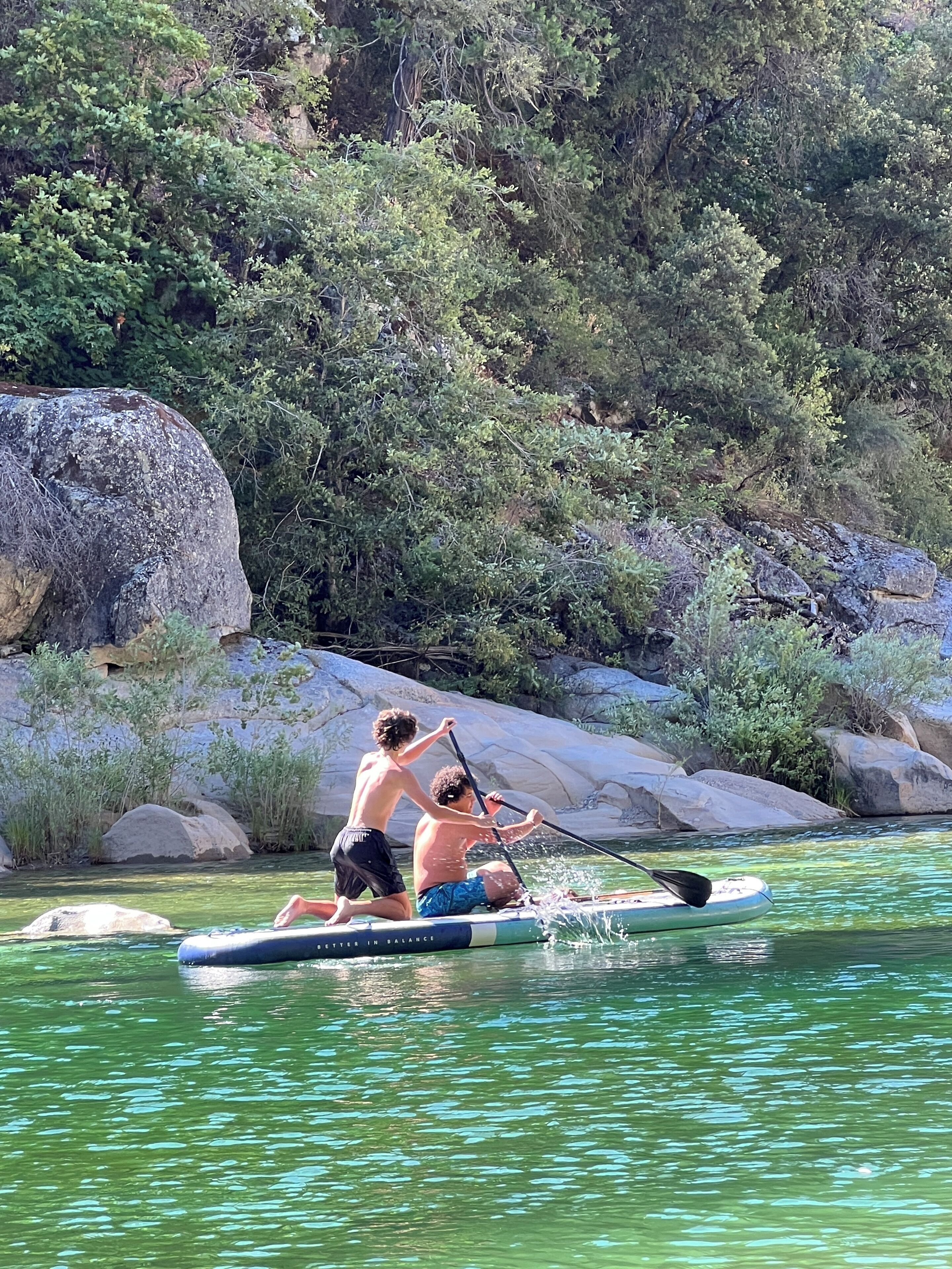 Dos personas en una tabla de remo en un río rodeado de rocas y follaje.
