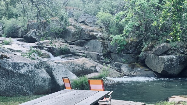 Une table de pique-nique avec deux chaises, située dans un cadre naturel, près d’une rivière et de rochers.
