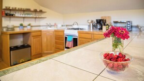 Une cuisine avec des meubles de rangement en bois, un plan de travail en marbre, un évier et un vase rempli de fleurs.