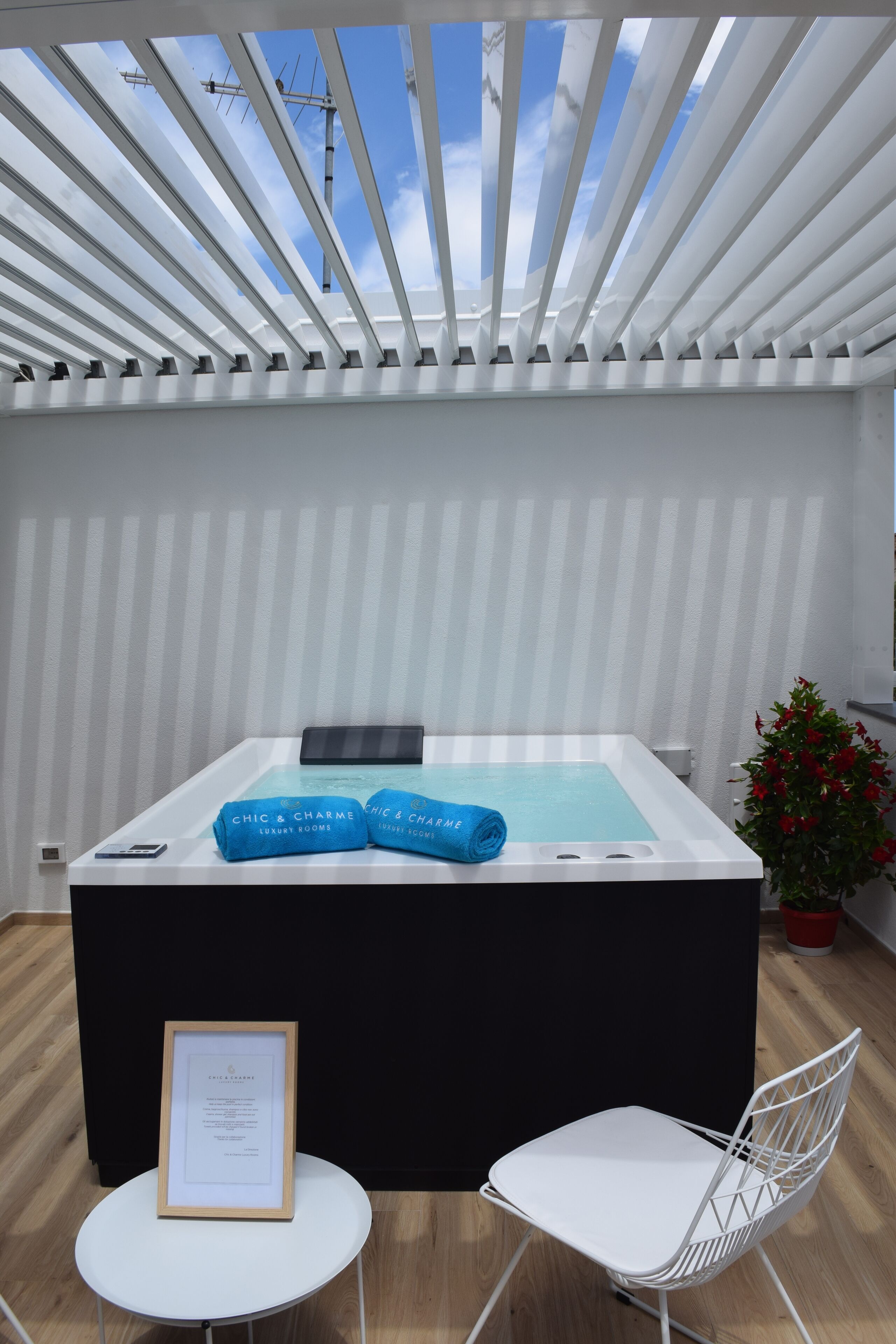 Zona de spa con un jacuzzi, dos toallas, un certificado enmarcado, una silla blanca y una planta en maceta.