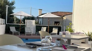Une terrasse extérieure avec une piscine, des meubles blancs et des parasols.