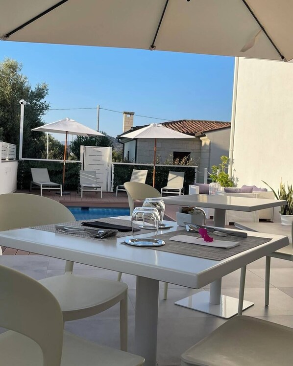 An outdoor patio with a pool, white furniture, and umbrellas. - Chic & Charme Luxury Rooms (Olbia)