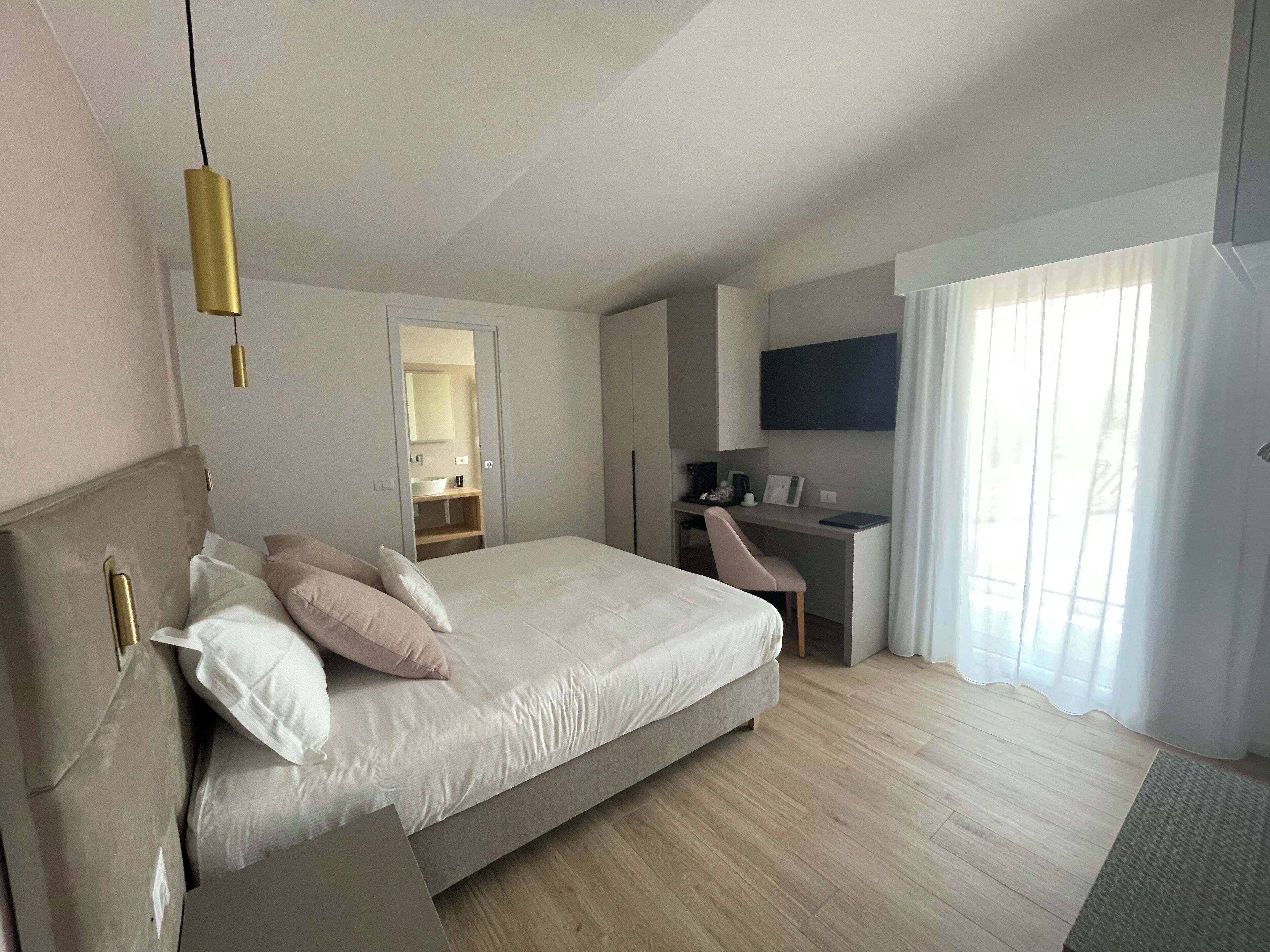Een moderne hotelkamer met een groot bed, een bureau, een stoel, een televisie en een badkamer zichtbaar door een geopende deur.