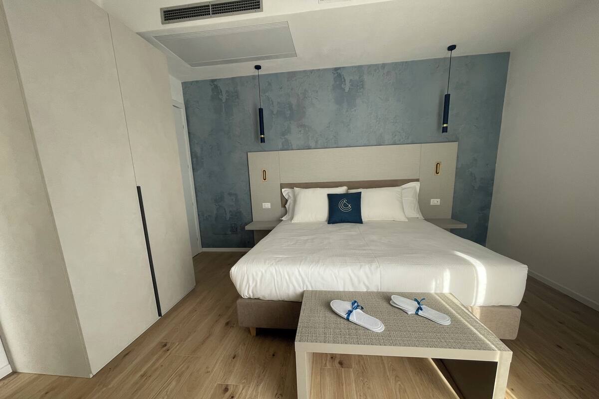 Een moderne hotelkamer met een groot bed, een klein tafeltje met slippers en een unieke, gestructureerde wand.