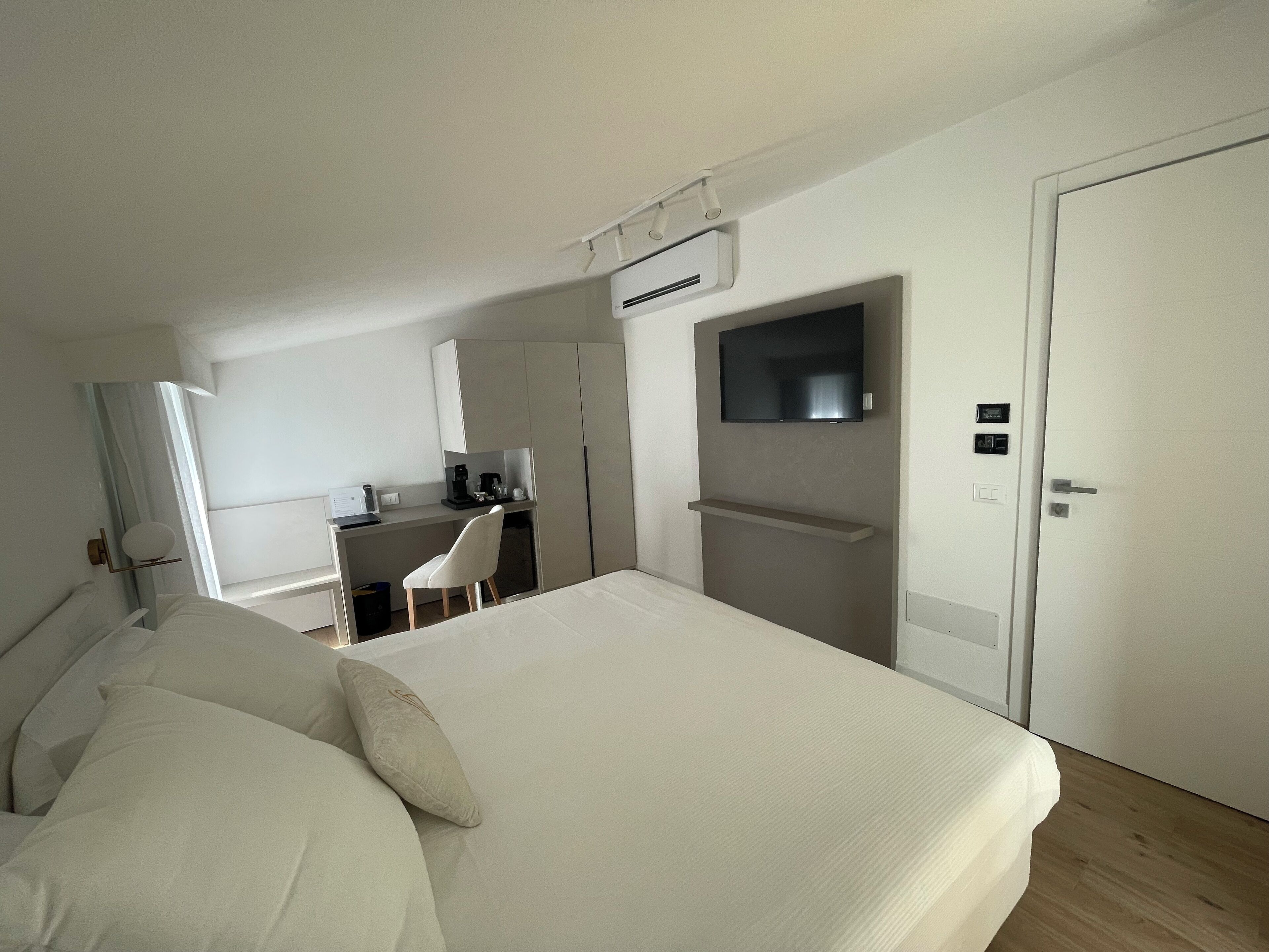 A modern hotel room with a large bed, a desk with a chair, a television mounted on the wall, and a door.