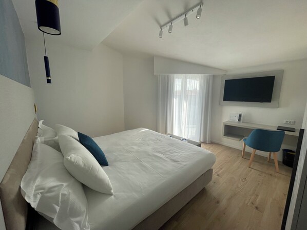 Une chambre d’hôtel moderne, dotée d’un grand lit, d’un bureau, d’une chaise et d’un téléviseur fixé au mur.