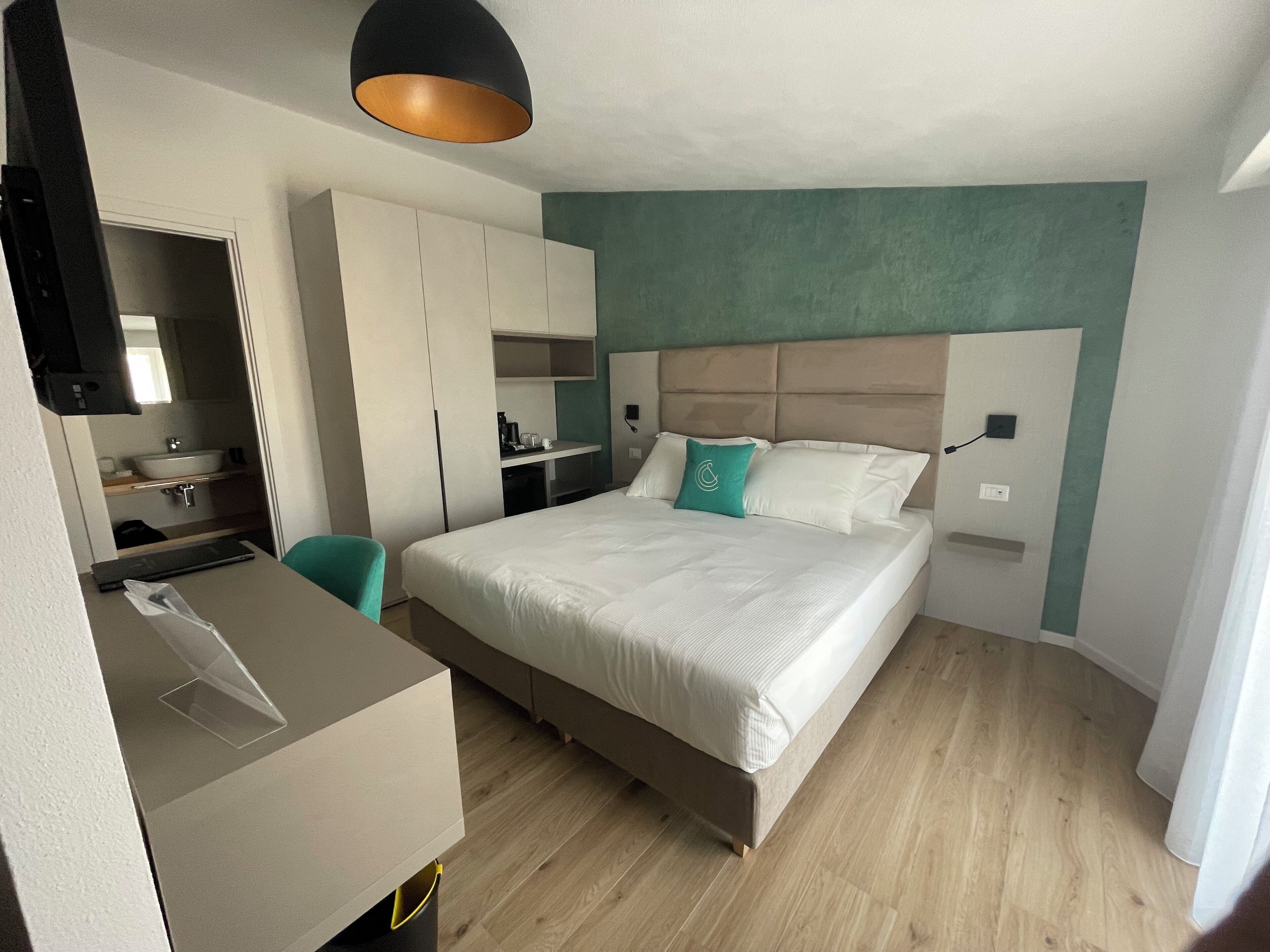 A modern hotel room with a bed, a desk, a wardrobe, and a bathroom.