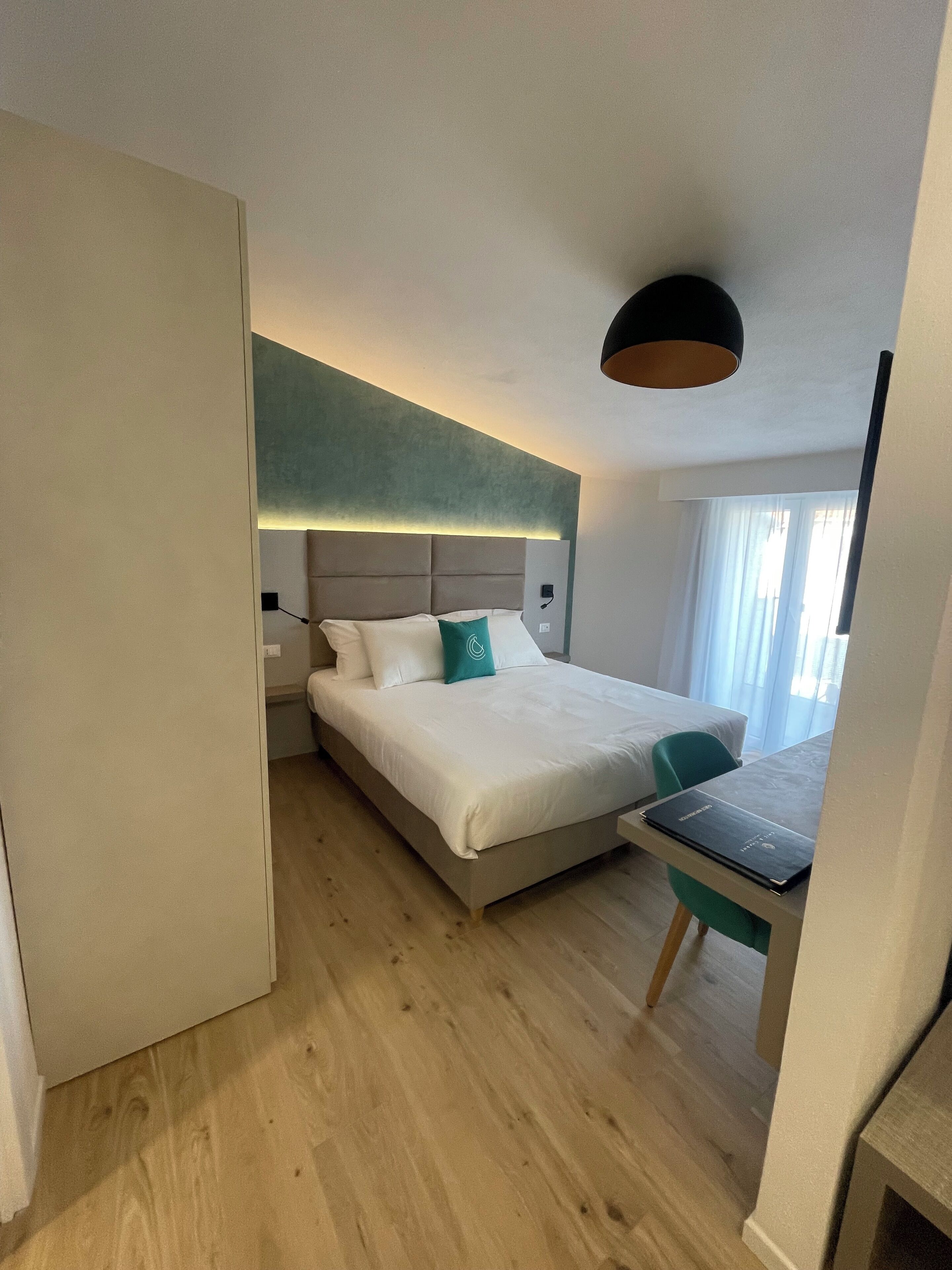 A modern hotel room with a large bed, a desk with a laptop, and a view of the outdoors through the window.